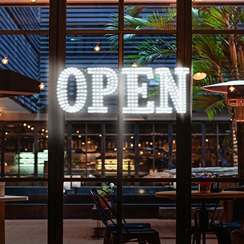 Illuminated open sign in restaurant window with outdoor seating.